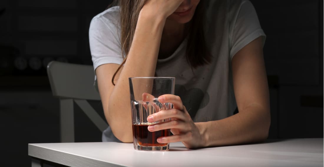 Женщина сидит на столом со стаканом алкоголя 